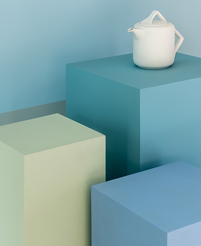 bule branco pilares azuis Um bule branco, de design moderno, está posicionado em cima de um de três pilares, cada qual em um tom diferente de azul, representando a versatilidade desta matiz.