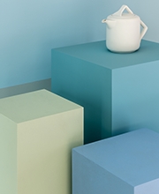 bule branco pilares azuis Um bule branco, de design moderno, está posicionado em cima de um de três pilares, cada qual em um tom diferente de azul, representando a versatilidade desta matiz.
