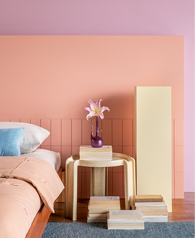 lirio quarto violetas Quarto tem cama arrumada, uma mesa de cabeceira apoiando um vaso e sua flor e, ao fundo paredes pintadas em tons calmos de violetas e rosas.